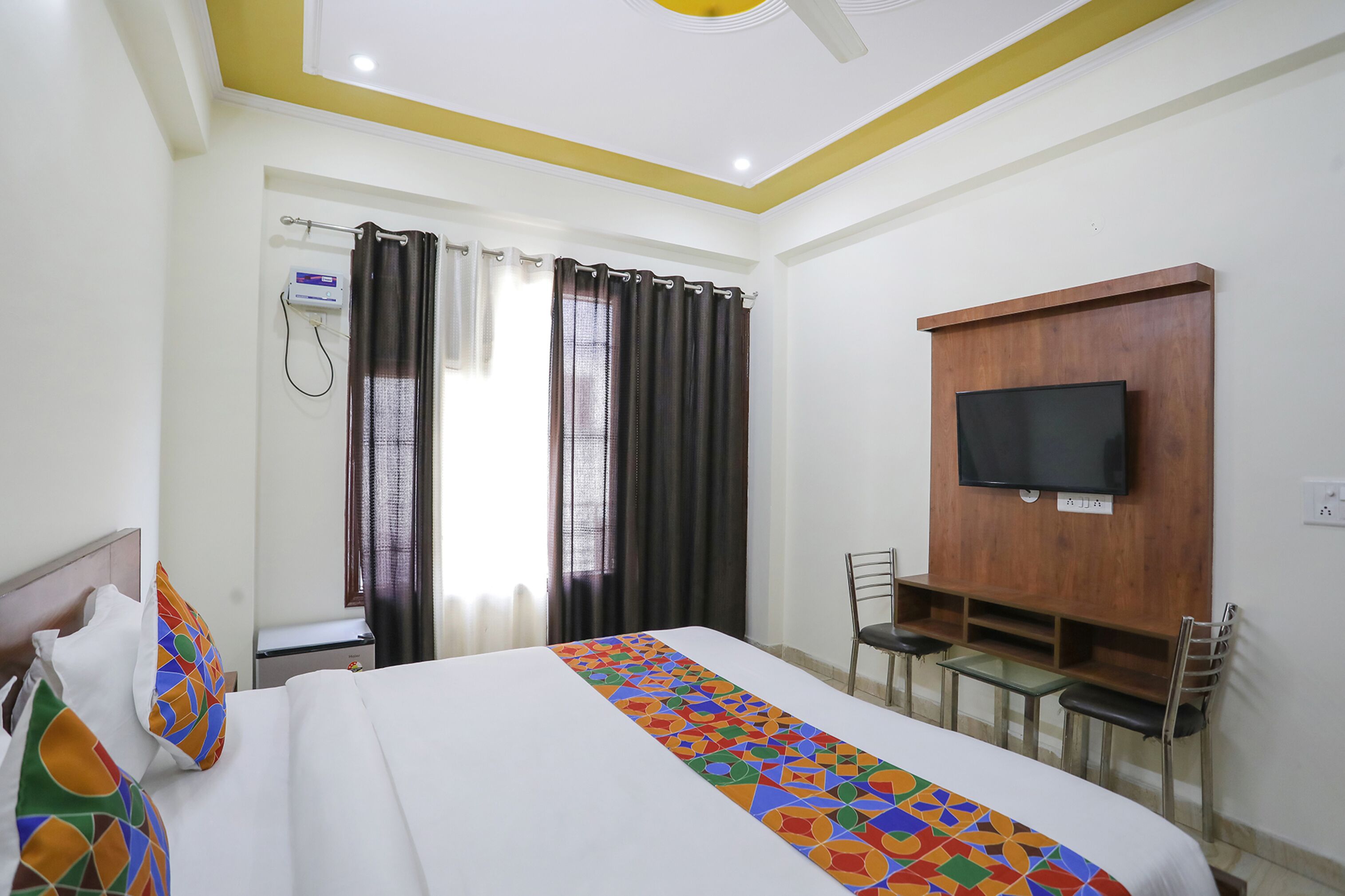A hotel room with a bed, a TV mounted on the wall, a desk with a chair, and a shower area.