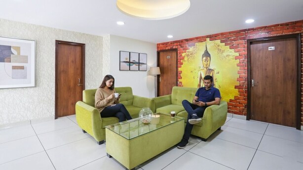 A reception area with two green sofas, a glass coffee table, and a Buddha mural on the wall. - FabHotel Star Corporate Suite I (Gurugram)