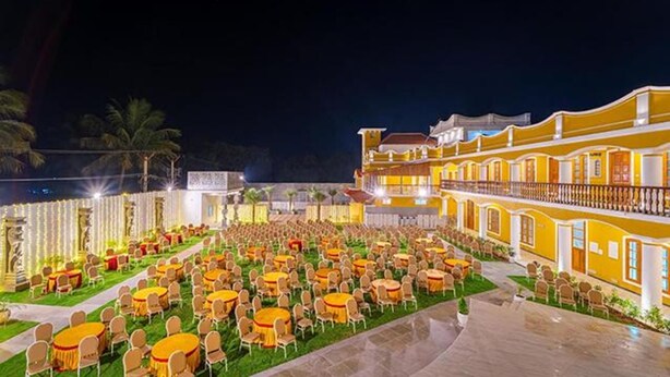 A hotel courtyard with multiple round tables and chairs, a large building with balconies, and palm trees in the background. - Fabhotel Prime Ar Phalazzo Resort (Vanur)