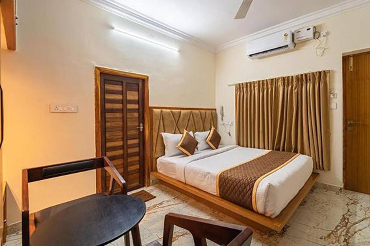 Une chambre d’hôtel avec un lit, un bureau et une chaise. Il y a une porte et un appareil de climatisation au mur.