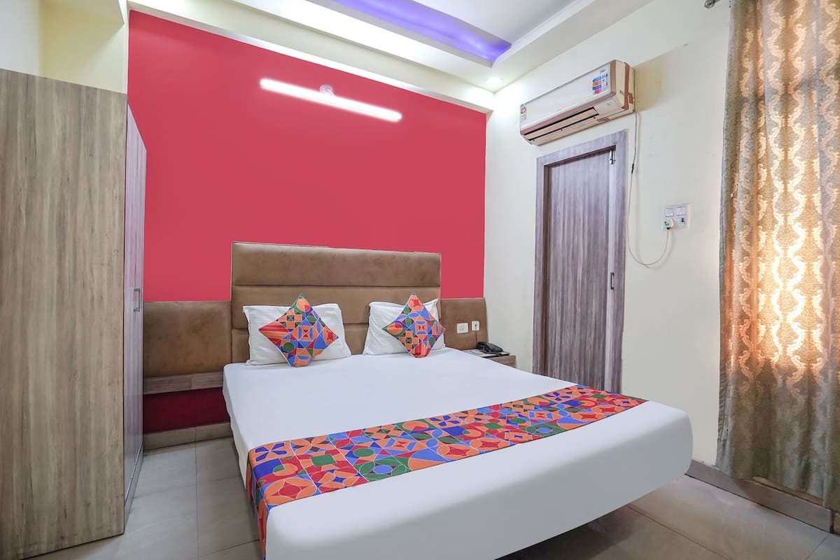 A hotel room with a large bed, a red accent wall, a wooden wardrobe, and an air conditioning unit.