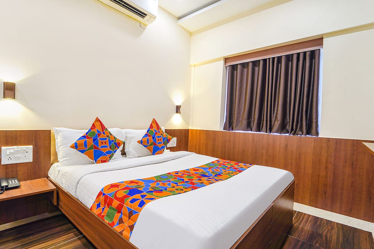 Quarto de hotel com cama, mesa de cabeceira, telefone e janela com cortinas.