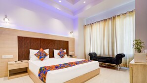 A modern hotel room with a large bed, a wooden headboard, a bedside table, a black sofa, and a large window with curtains. - Fabhotel Interglobe Oasis (Gurugram)