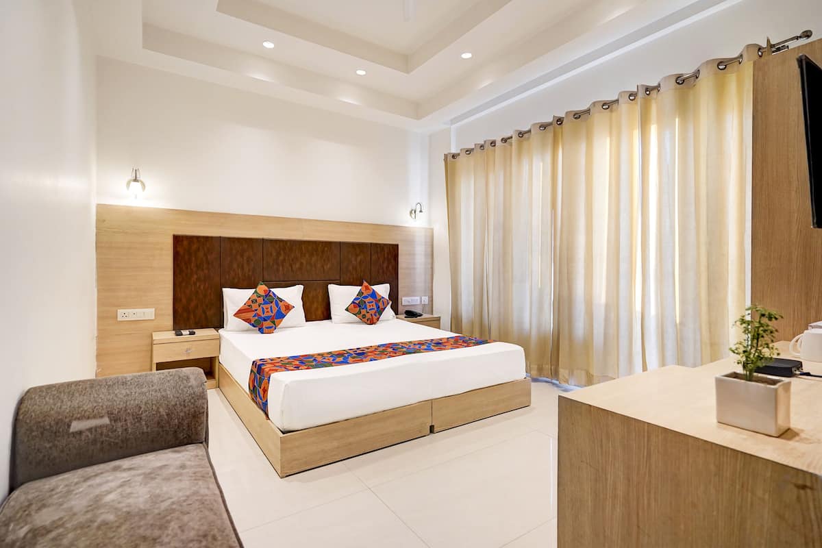 A modern hotel room with a large bed, wooden headboard, bedside tables, a desk, and a potted plant.