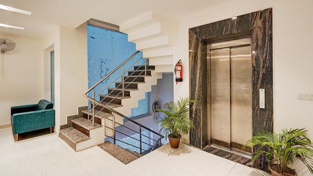 A modern interior with a staircase, a blue accent wall, a reception desk, and an elevator. - Fabhotel Interglobe Oasis (Gurugram)