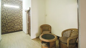 Un pasillo con papel tapiz estampado, una silla de mimbre, una mesita y una puerta que da a otra habitación.