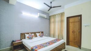 Un dormitorio con cama, mesita de noche, aire acondicionado, ventilador de techo, cortinas y una puerta de madera.