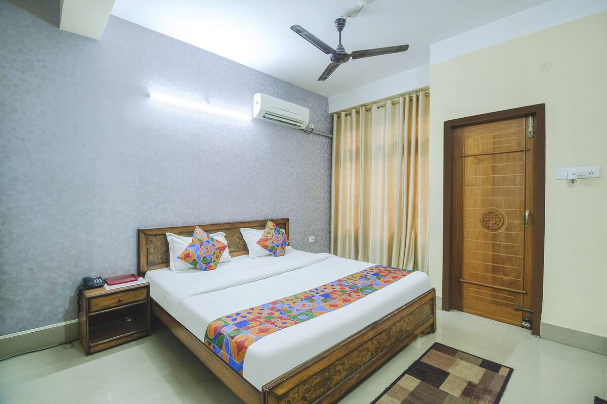 Un dormitorio con cama, mesita de noche, aire acondicionado, ventilador de techo, cortinas y una puerta de madera.