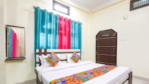Una cama bien hecha con un edredón colorido, una ventana con cortinas y un armario de madera.