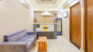 Zona de recepción de un hotel con un sofá, una mesa de madera y un mostrador de recepción con un cartel que dice "Tab Hotels".