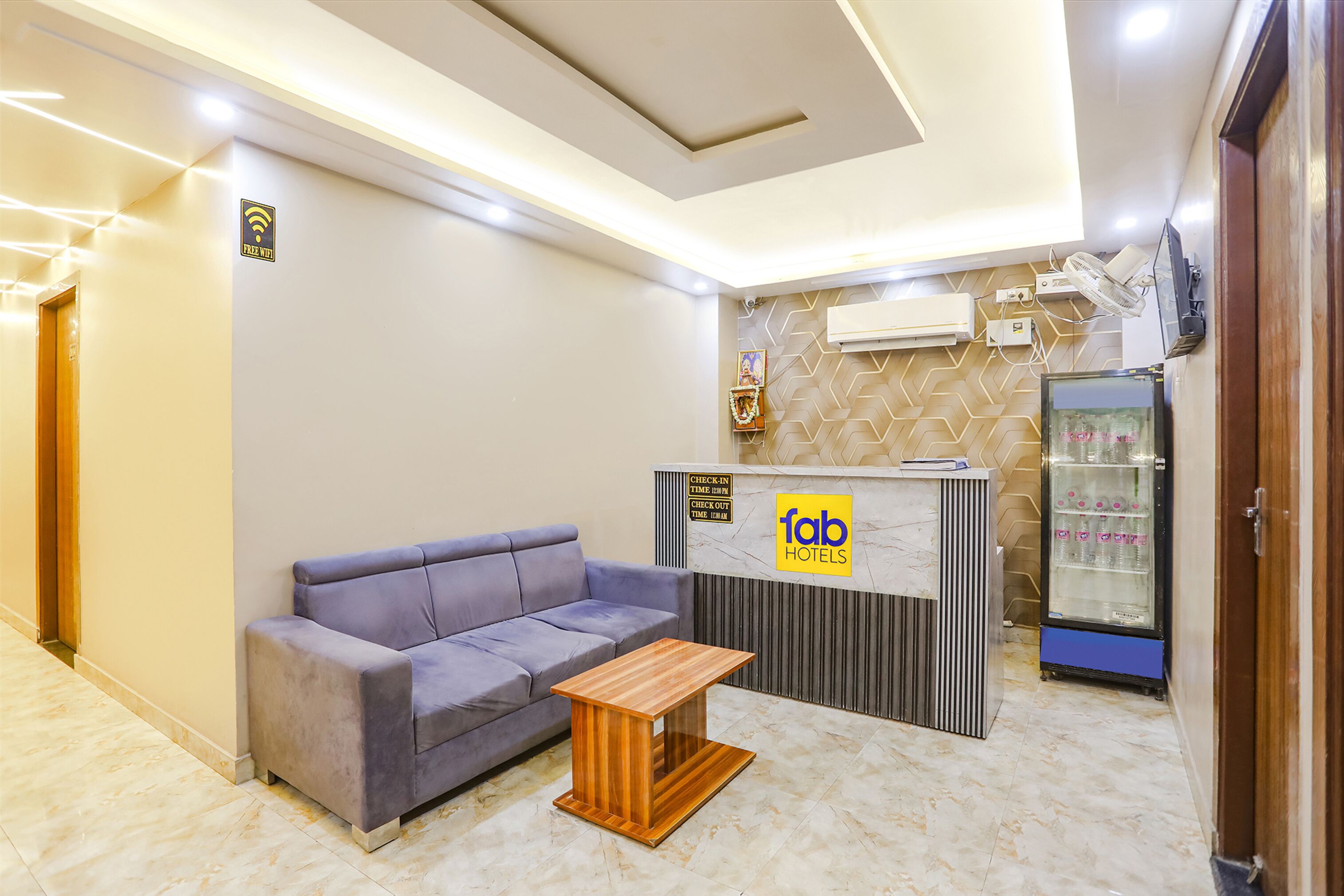 Zona de recepción con sofá, mesa de madera, mostrador de recepción y máquina expendedora.