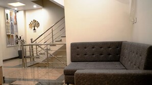 A lobby with a grey sofa, a staircase, and a wall-mounted tree decoration. - FabHotel Ramana (Udaipur)