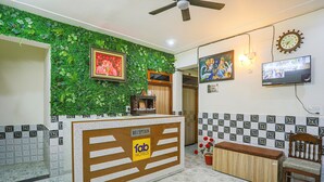A reception area with a green wall, a reception desk, a television, and a clock. - Fabexpress Dau Ji Residency (Mathura)