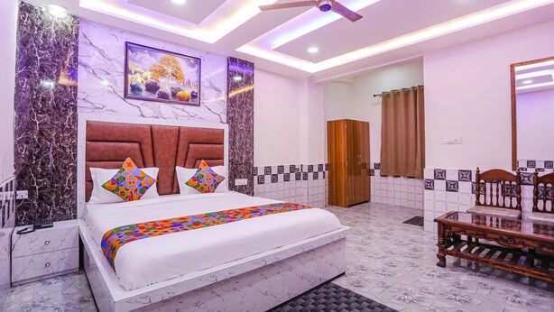 A modern bedroom with a large bed, a ceiling fan, and a bathroom visible through an open door. - Fabexpress Dau Ji Residency (Mathura)