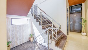 Escadaria moderna com guarda-corrimão de metal, parede de mármore e um vaso de planta.