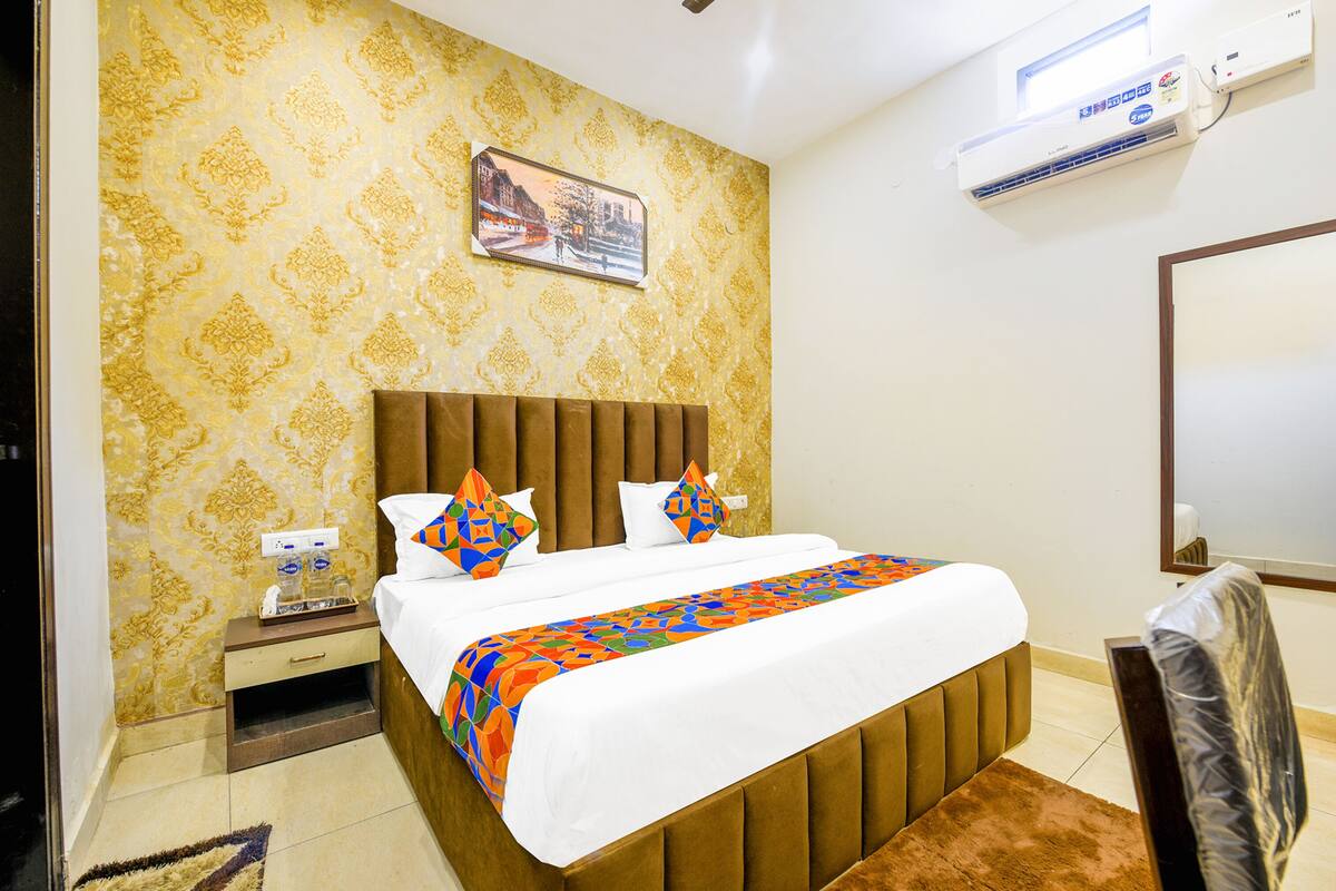 A hotel room with a bed, a nightstand, a mirror, and an air conditioning unit.