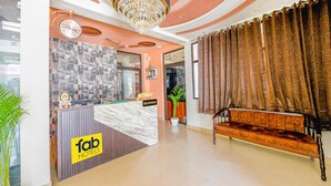 Uma área de recepção de hotel com balcão de mármore, um relógio, um candelabro e um sofá.