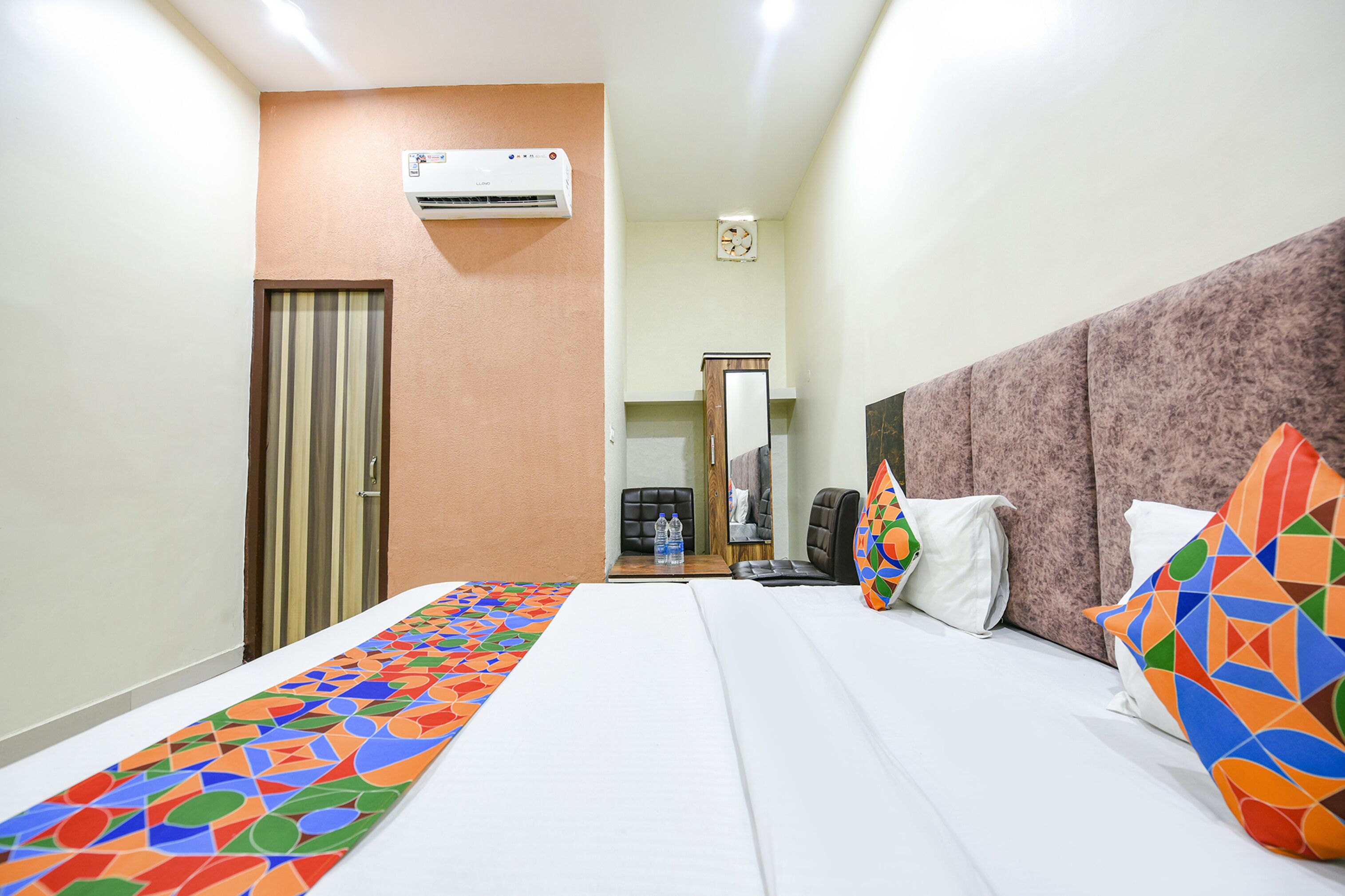 Quarto de hotel com cama, escrivaninha, ar condicionado, espelho e porta.