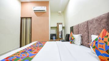 Quarto de hotel com cama, escrivaninha, ar condicionado, espelho e porta.