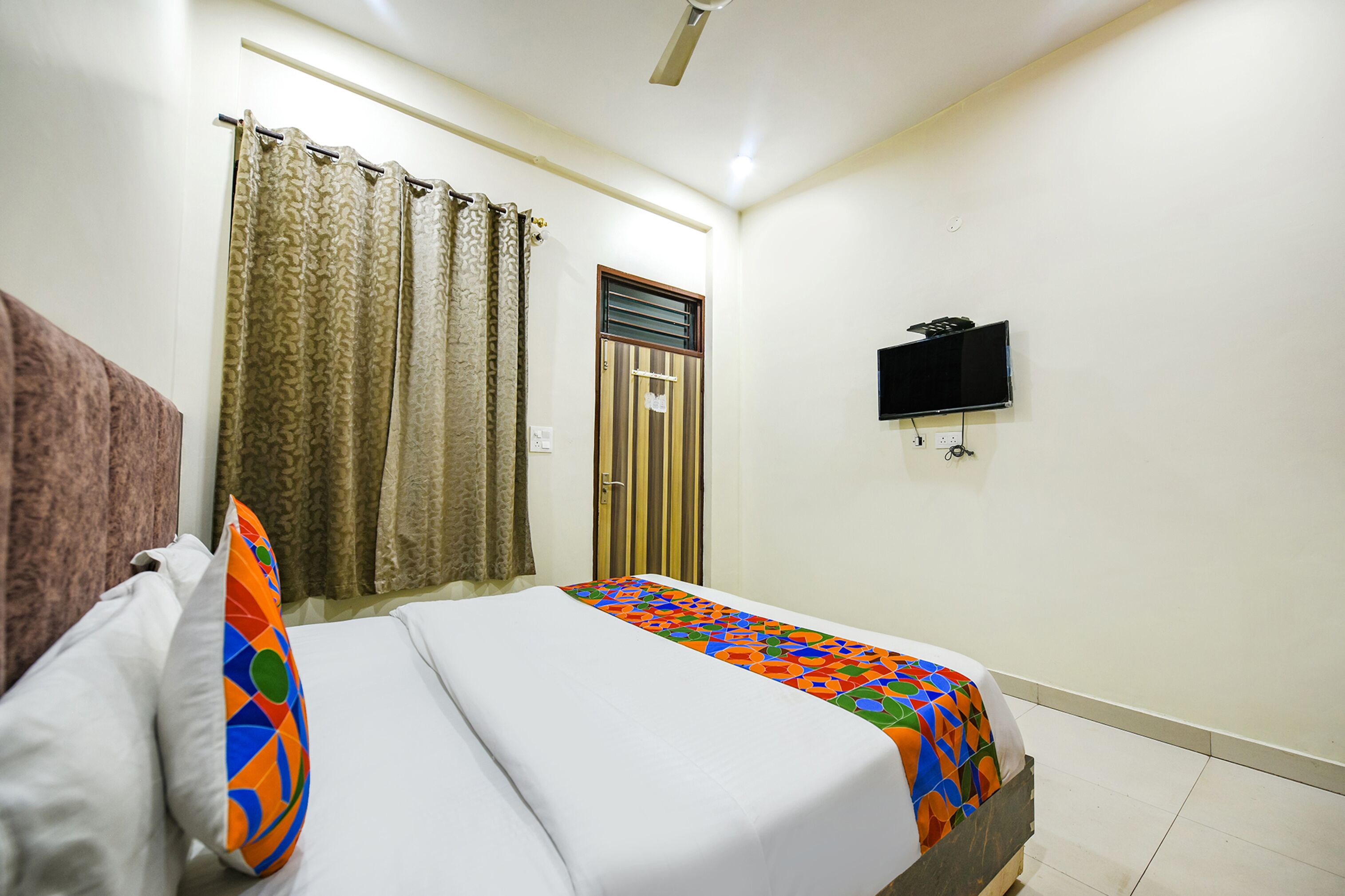 A hotel room with a bed, curtains, a television, and a door.