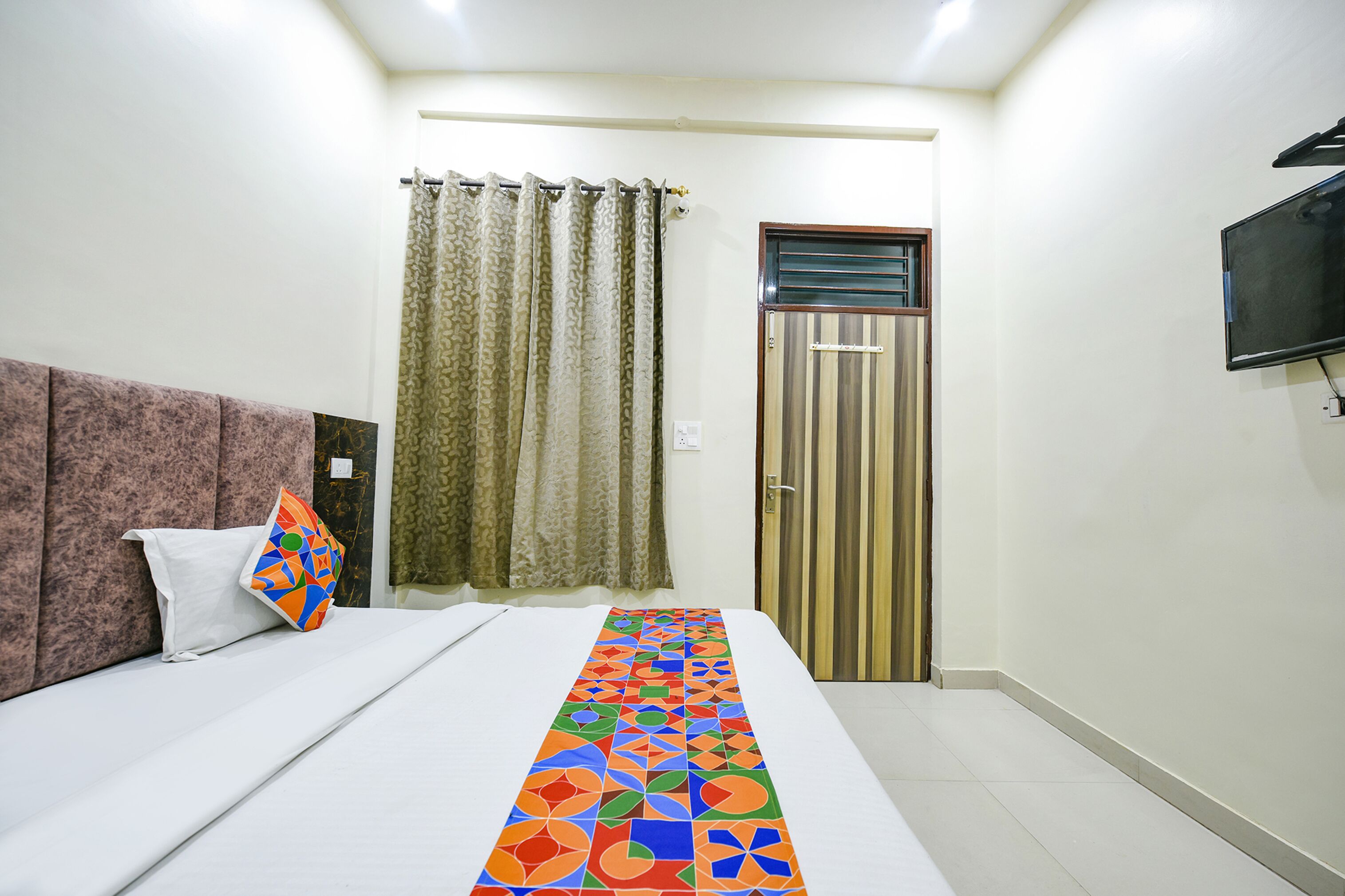 A hotel room with a bed, a TV mounted on the wall, a curtain, and a door.