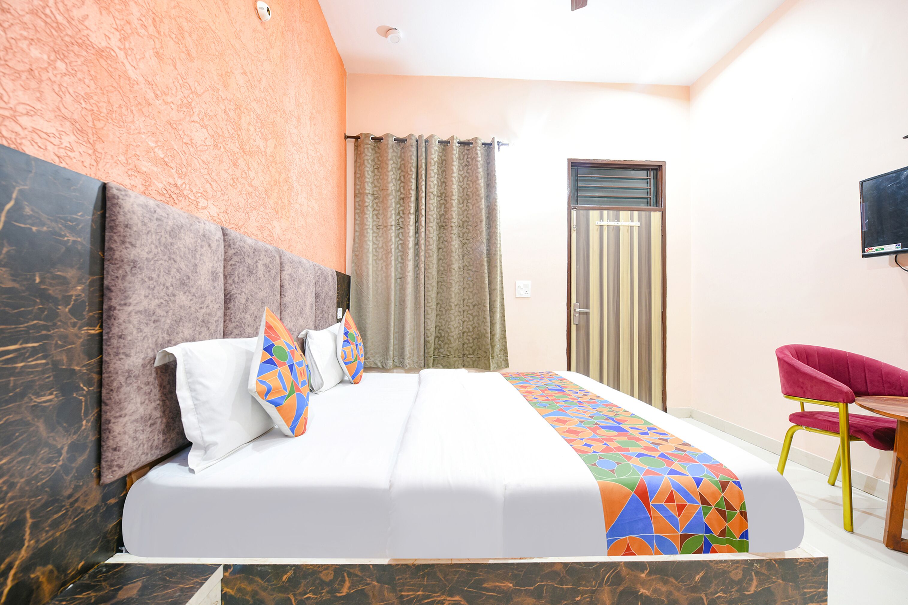 A hotel room with a large bed, a TV mounted on the wall, and a small table with a chair.