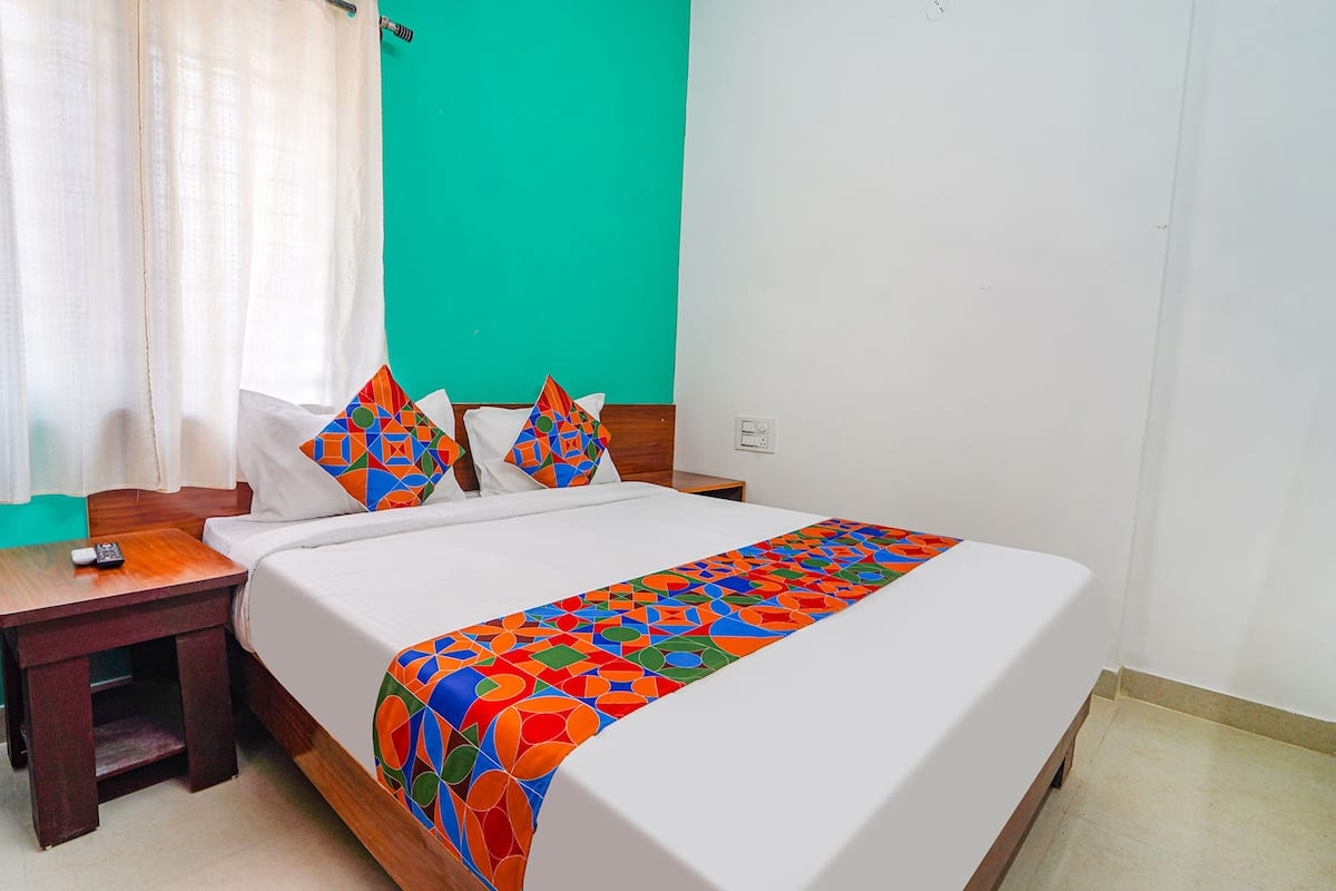 A hotel room with a bed, a nightstand, a remote control, and a teal-colored wall.