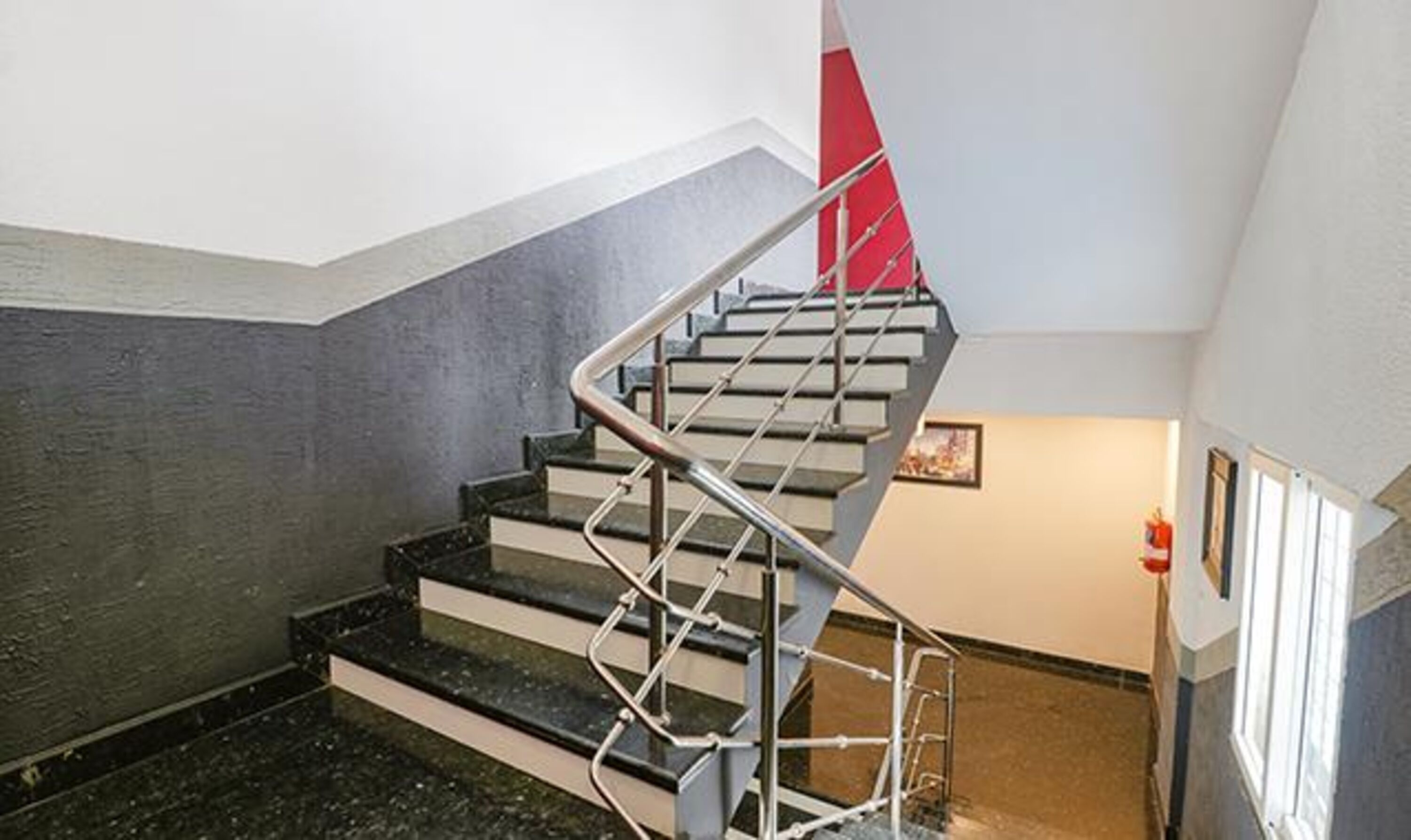 Una escala amb barana metàl·lica i un detall vermell a la paret.