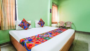 Een netjes opgemaakt bed met een kleurrijk sprei, twee kussens en een stoel in een kamer met groene wanden en een raam met gordijnen.