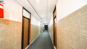 A hallway with patterned walls, a carpeted floor, and a fire extinguisher on the left. - Fabexpress Golden Stone (Ghaziabad)