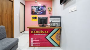 Een hotel receptie met een roze muur, een groot televisiescherm en een houten receptiebalie.