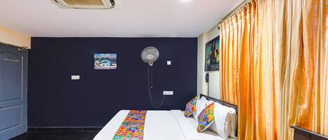 A hotel room with a bed, a bedside table, a fan, and a curtain.