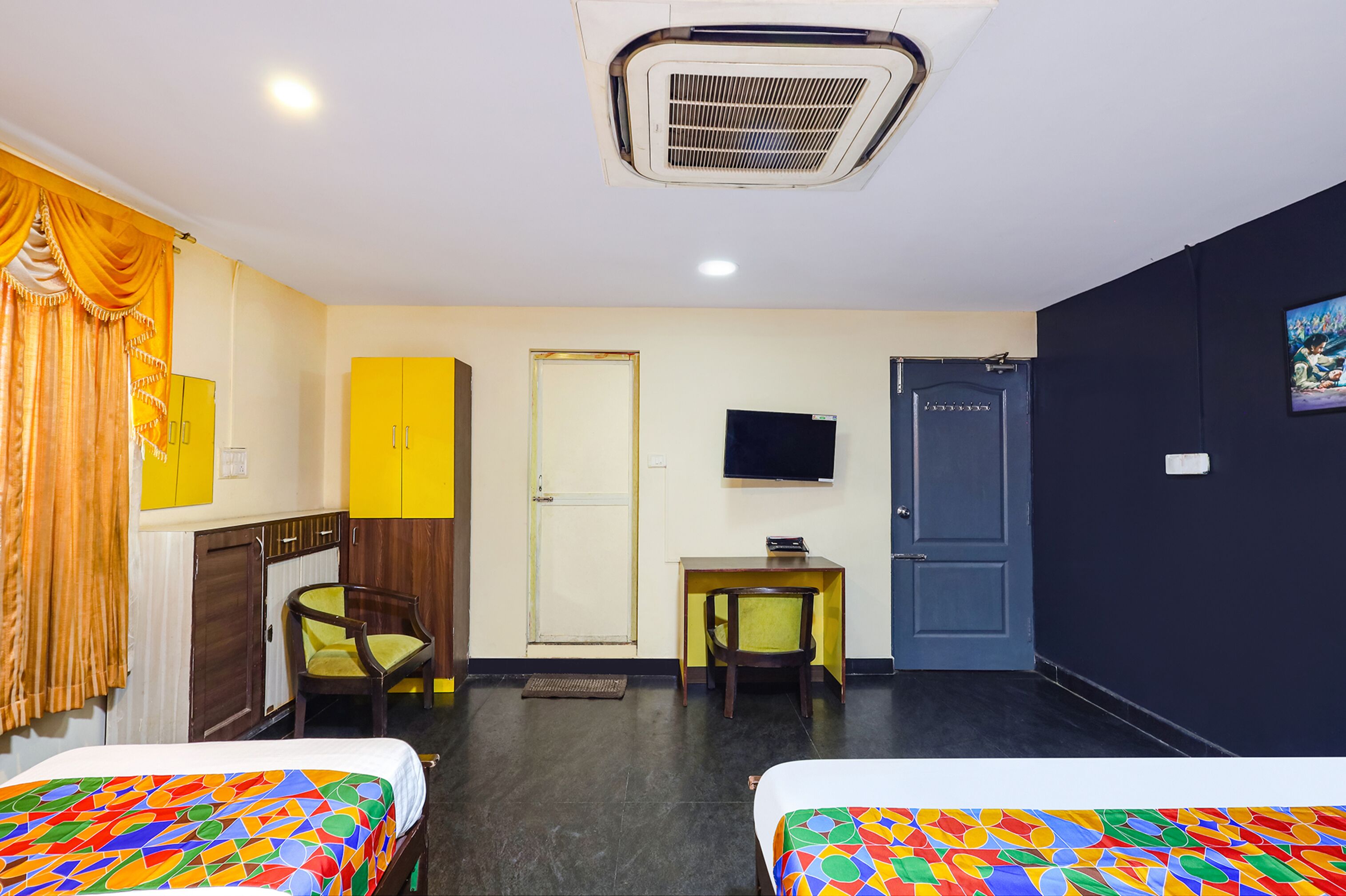 A hotel room with two beds, a desk, a chair, a television, and a wardrobe.
