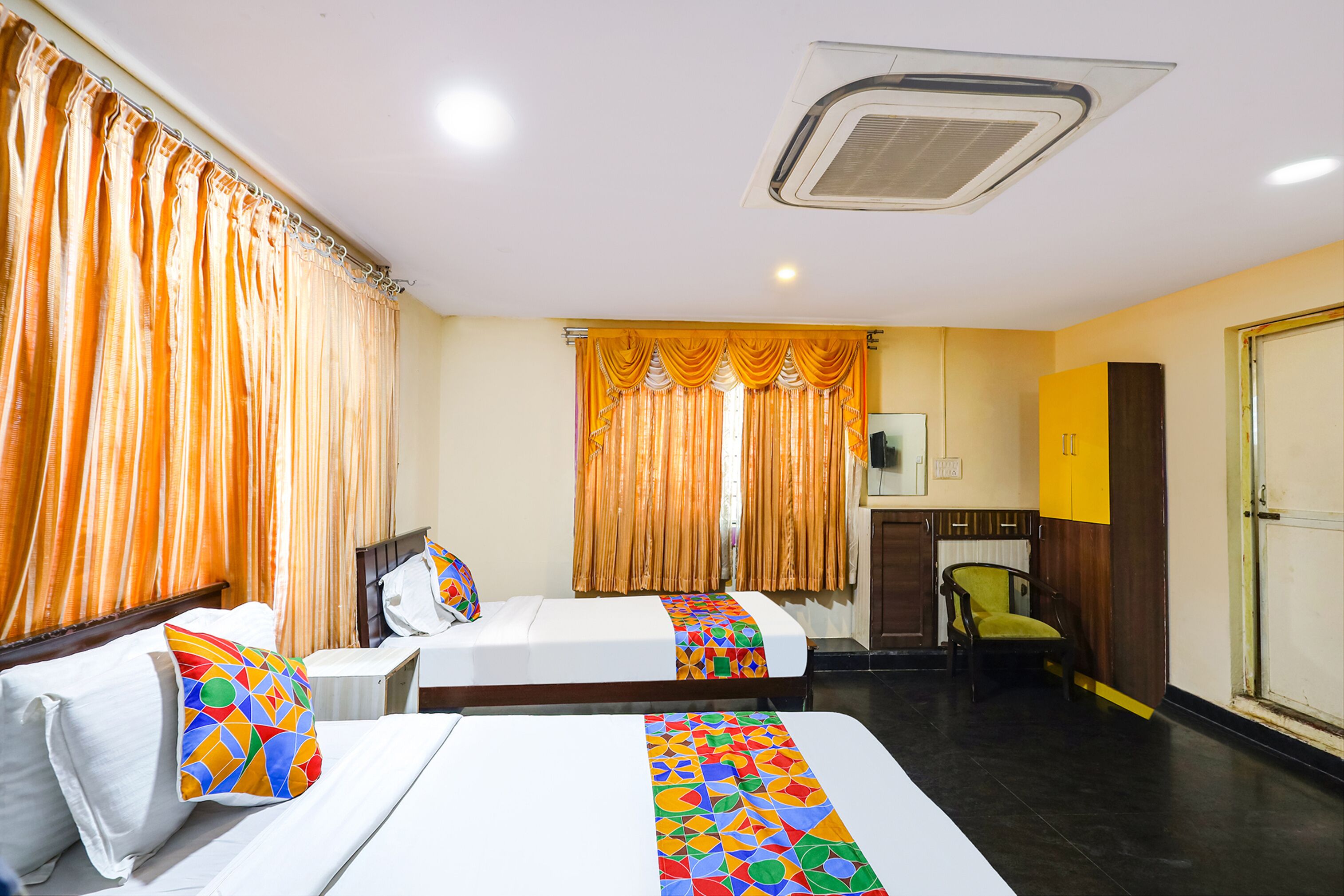 A hotel room with two beds, a wooden wardrobe, a chair, and a television.