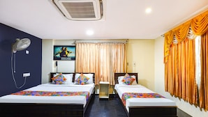 A hotel room with two beds, a ceiling fan, a wall-mounted air conditioner, and a window with curtains. - Fabexpress India Gate (Chennai)