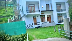 A multi-story building with balconies, a green lawn, and a construction site in the background. - Fabhotel Prime D Grand (Kodaikanal)