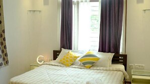 A hotel room with a bed, a bedside table with a lamp, and a window with curtains. - Fabhotel Prime D Grand (Kodaikanal)