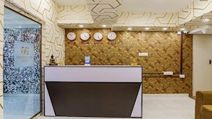 A reception area with a modern design, featuring a reception desk, a wall clock, and a decorative wall pattern. - Fabhotel Prime D Grand (Kodaikanal)