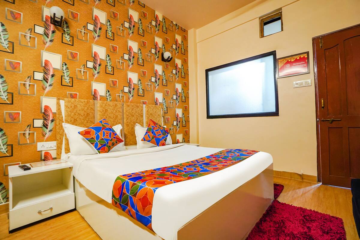 A neatly arranged hotel room with a bed, a nightstand, a TV, and a door.