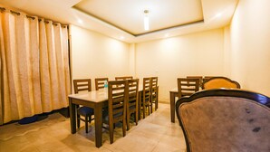 Uma sala de jantar com uma mesa, cadeiras, uma luminária no teto e uma cortina.