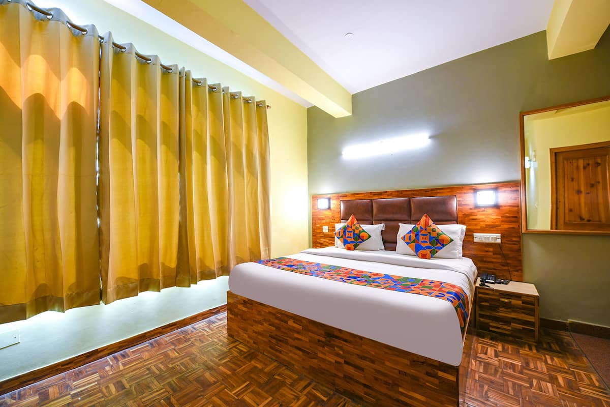 Une chambre d’hôtel avec une tête de lit en bois, un lit avec une literie à motifs, une table de chevet et un plancher en bois.