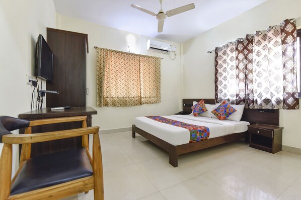 A bedroom with a bed, a desk, a chair, a ceiling fan, and curtains. - Fabexpress Clausil Inn (Panaji)
