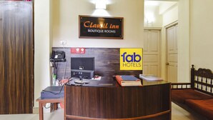 Ein Empfangsschalter mit einem Schild für 'Clamil Inn Boutique Rooms' und einem 'fab hotels' Logo. Ein Telefon, ein Computer und ein kleiner Tisch mit Gegenständen darauf sind vorhanden.