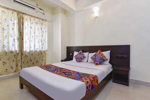 A neatly made bed with a colorful bedspread, a wooden headboard, and a bedside table with a lamp. - Fabexpress Clausil Inn (Panaji)