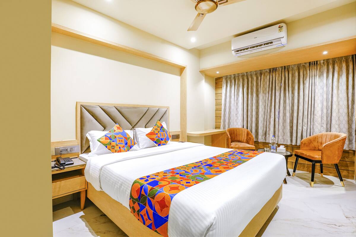A hotel room with a large bed, a bedside table with a phone, a chair, and a desk with a chair.