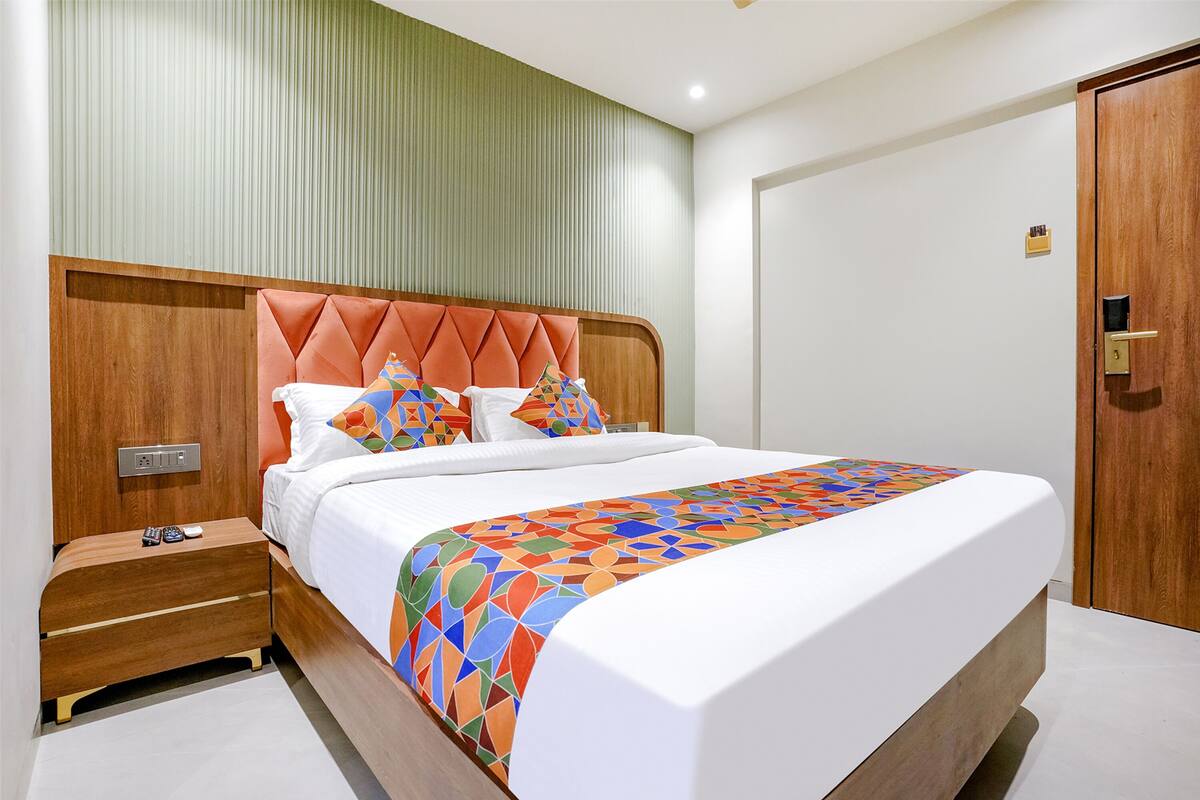 A modern hotel room with a wooden headboard, a neatly made bed, a bedside table with a remote control, and a door with a key lock.