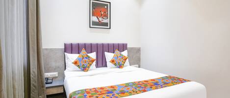 Habitación de hotel con cama, cabecera, mesita de noche, teléfono, una obra de arte en la pared y ventana con cortinas.