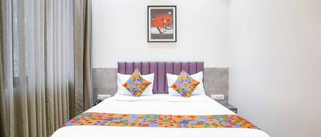 A modern hotel room with a large bed, a purple headboard, and a colorful geometric-patterned bedspread.