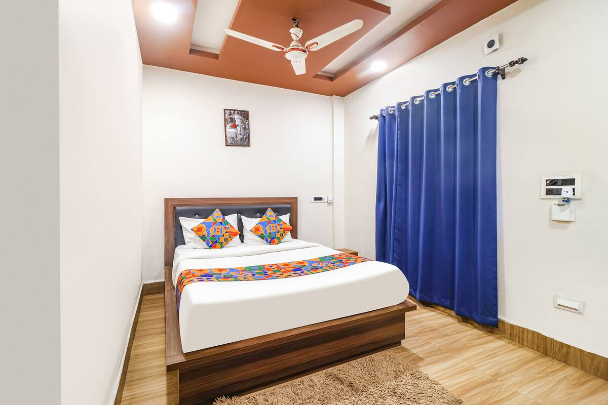 A bedroom with a bed, a ceiling fan, a blue curtain, and a wall-mounted air conditioning unit.