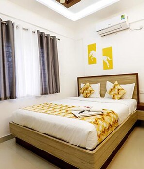 A bedroom with a large bed, a window with curtains, an air conditioning unit, and two yellow wall art pieces. - Fabhotel Marella Suites (Bengaluru)